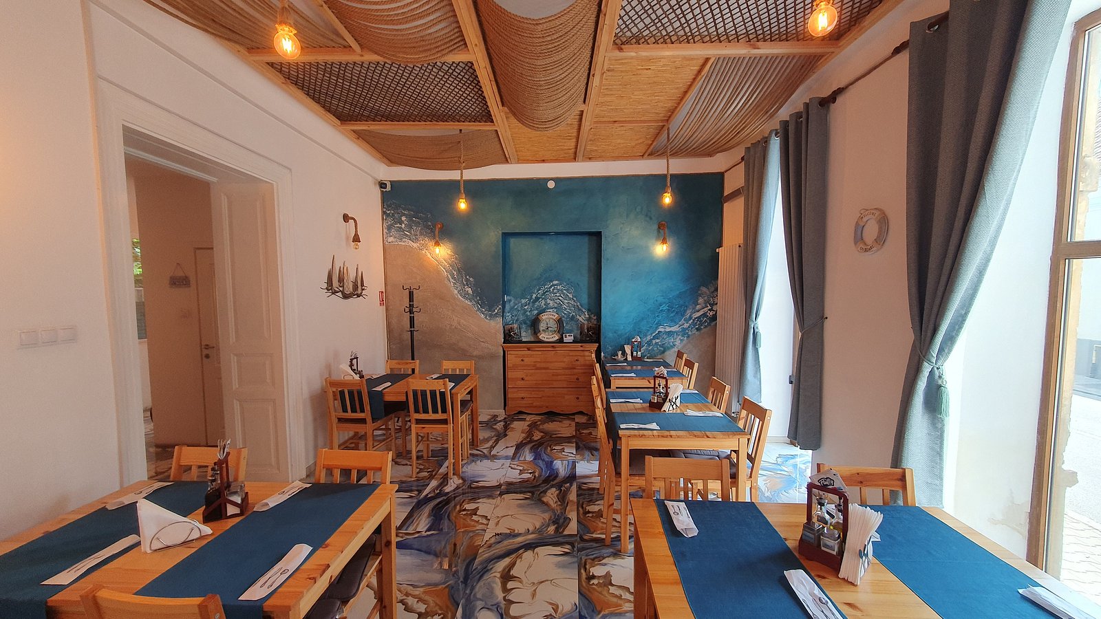 Sala cu pereți albaștri, mese lungi și tavan de frânghie