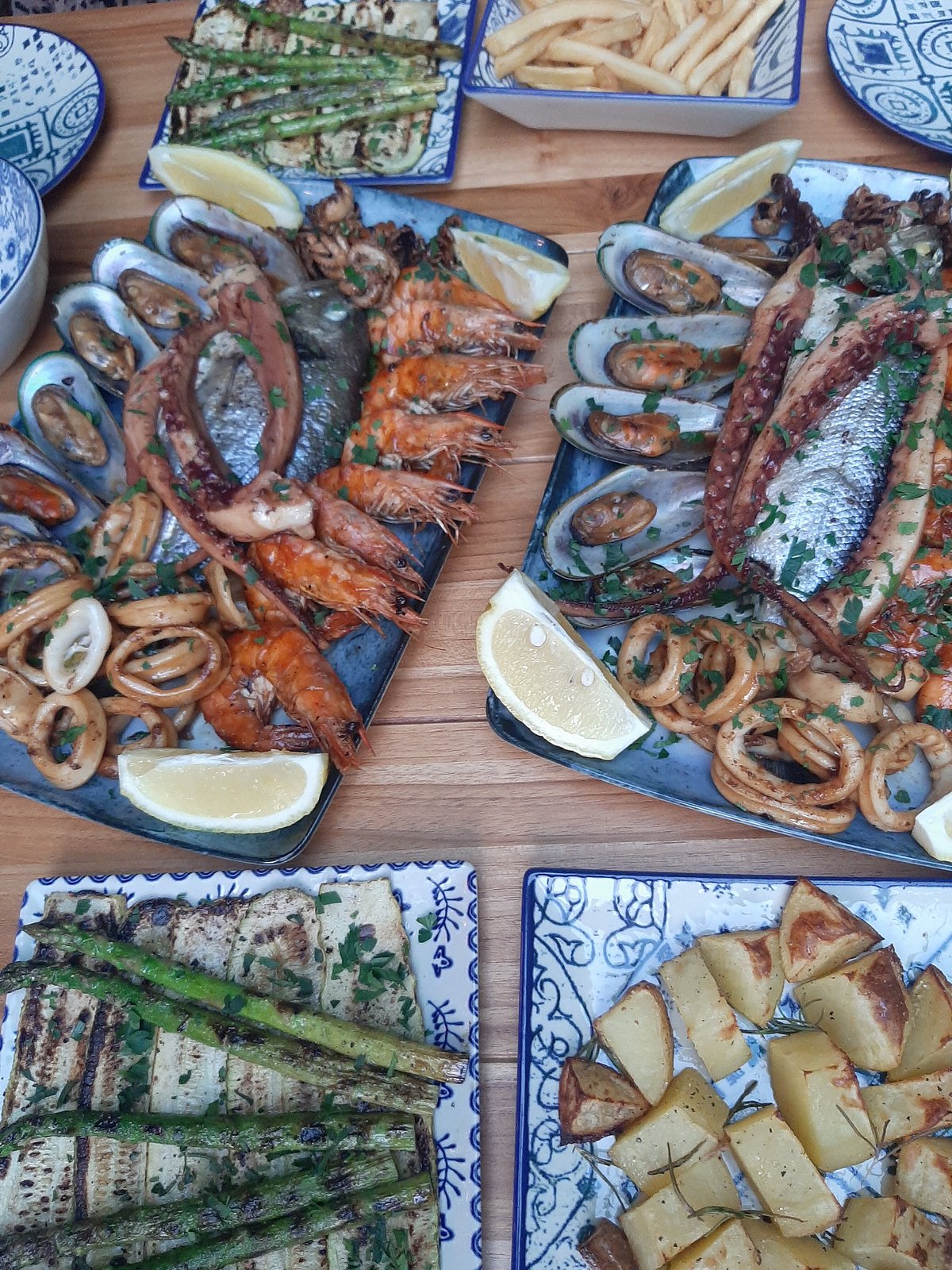 Un platou mare cu creveți, midii, inele de calamar și tentacule de caracatiță, cu farfurii separate de sparanghel și cartofi